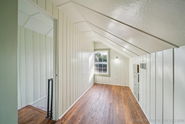 bonus room with a textured ceiling, lofted ceiling, wood walls, and dark hardwood / wood-style floors