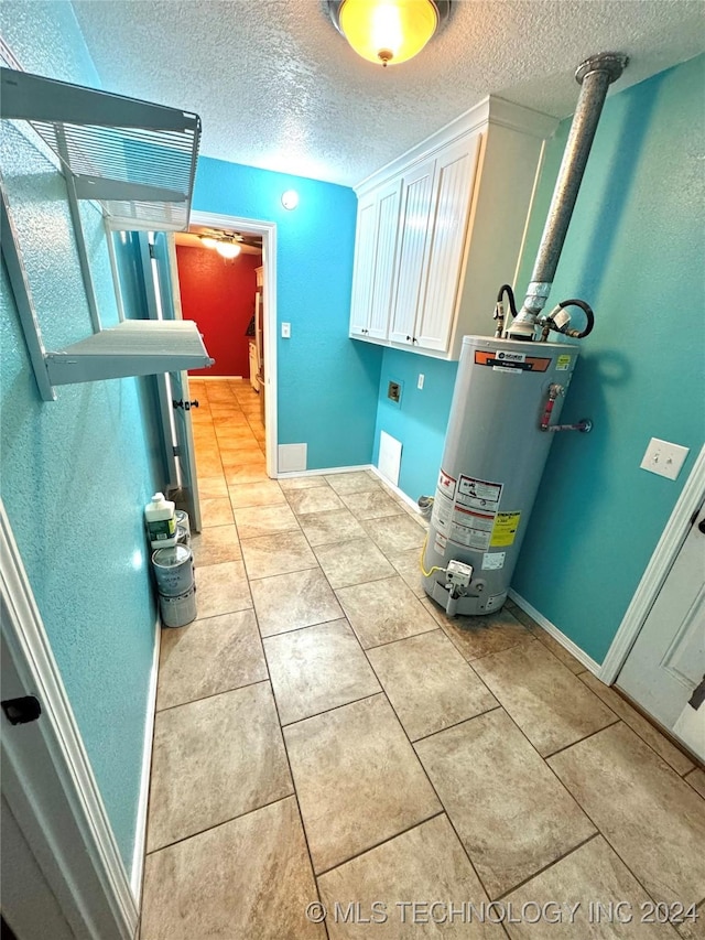 laundry room with cabinets, gas water heater, light tile patterned floors, and a textured ceiling