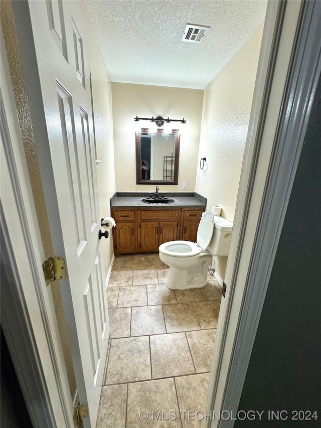 bathroom featuring tile patterned flooring, vanity, a textured ceiling, and toilet