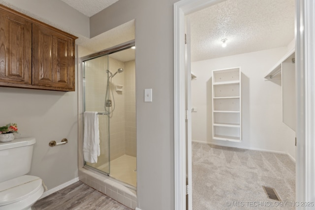 full bathroom with visible vents, toilet, a textured ceiling, a shower stall, and baseboards