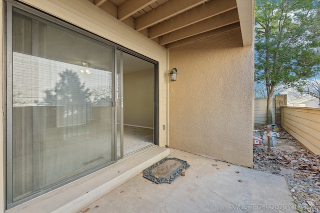 view of exterior entry featuring stucco siding and fence