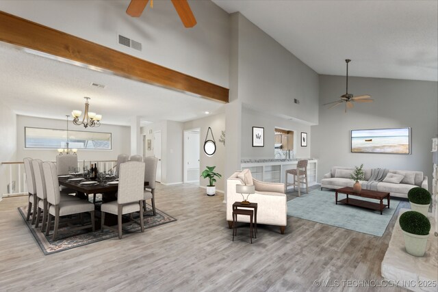 living area featuring ceiling fan with notable chandelier, wood finished floors, visible vents, and high vaulted ceiling