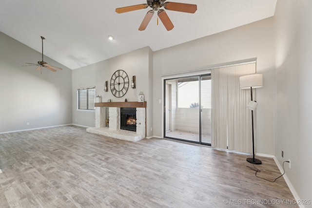 unfurnished living room featuring a ceiling fan, wood finished floors, baseboards, high vaulted ceiling, and a warm lit fireplace