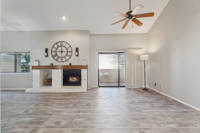 unfurnished living room with wood finished floors, baseboards, a warm lit fireplace, and ceiling fan