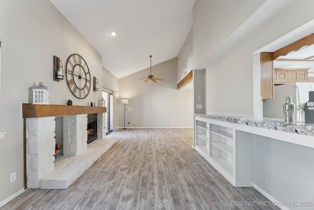 unfurnished living room featuring baseboards, a stone fireplace, wood finished floors, high vaulted ceiling, and a ceiling fan