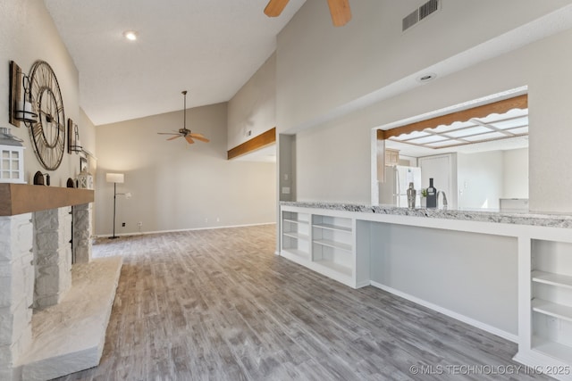 unfurnished living room with visible vents, built in shelves, a stone fireplace, wood finished floors, and a ceiling fan