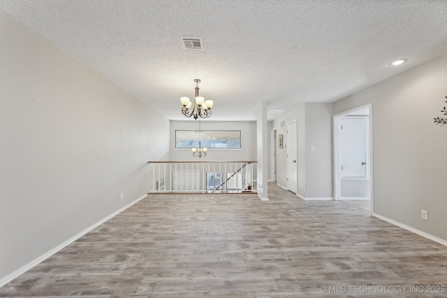 unfurnished room with wood finished floors, visible vents, baseboards, an inviting chandelier, and a textured ceiling