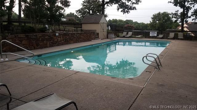 pool with fence, an outdoor structure, a shed, and a patio area