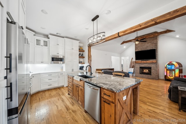 kitchen featuring stainless steel appliances, lofted ceiling with beams, an island with sink, white cabinets, and ceiling fan with notable chandelier