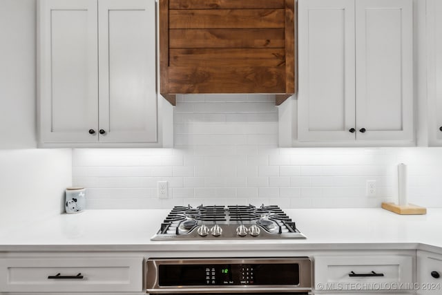 kitchen with decorative backsplash, white cabinetry, stainless steel appliances, and premium range hood