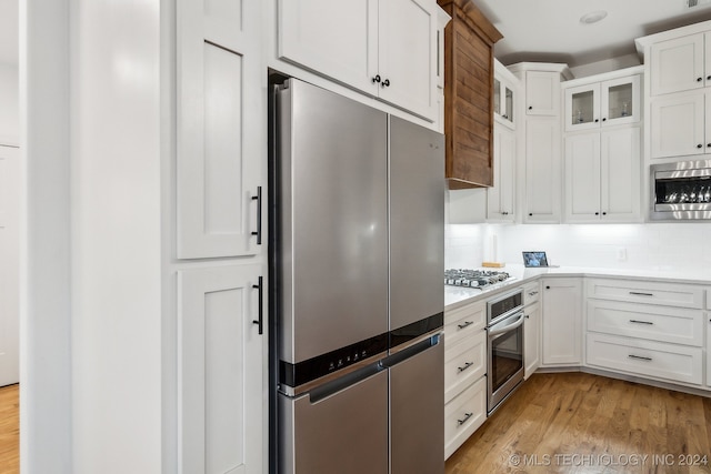 kitchen with white cabinets, decorative backsplash, stainless steel appliances, and light hardwood / wood-style flooring