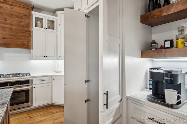 kitchen with appliances with stainless steel finishes, light hardwood / wood-style flooring, white cabinetry, and tasteful backsplash