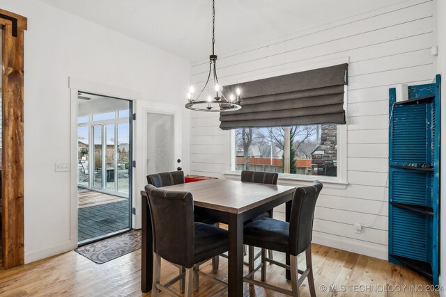 dining room with an inviting chandelier, light hardwood / wood-style flooring, and wood walls