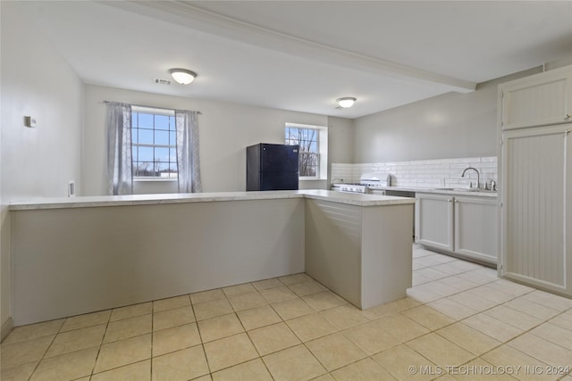 kitchen featuring black refrigerator, white cabinetry, a wealth of natural light, and tasteful backsplash