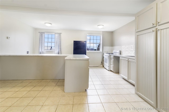 kitchen with white range with gas cooktop, black fridge, decorative backsplash, and a wealth of natural light