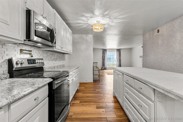 kitchen featuring white cabinets, wood-type flooring, stainless steel appliances, and light stone countertops