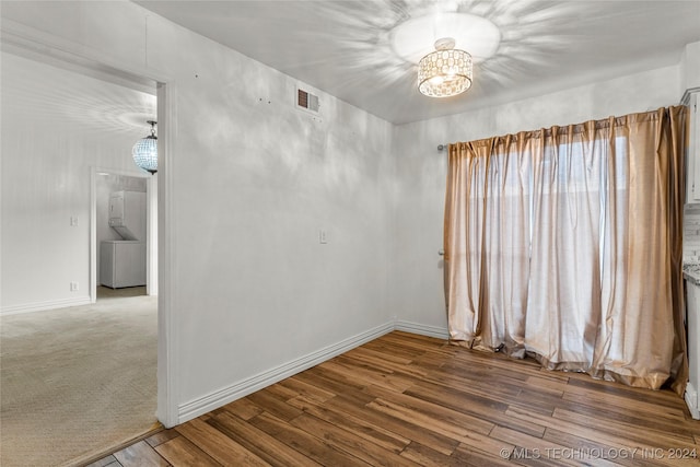 empty room featuring washer / dryer, wood-type flooring, and a notable chandelier