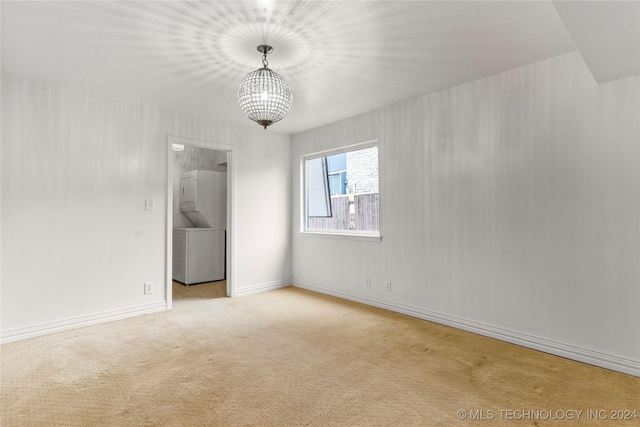 carpeted empty room with a chandelier and stacked washer / drying machine