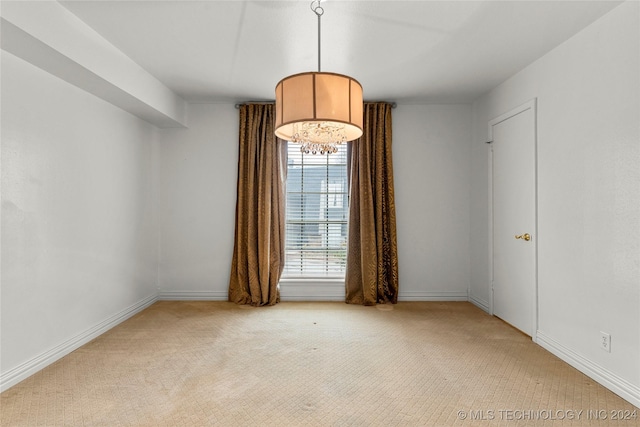 empty room featuring a chandelier and light colored carpet