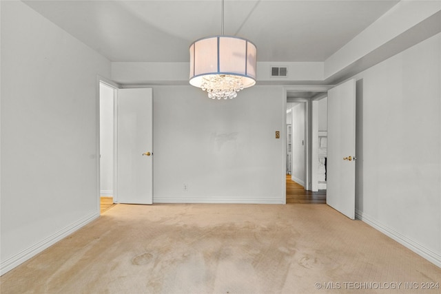 carpeted spare room featuring a chandelier