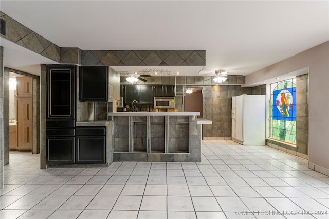 kitchen featuring white refrigerator, sink, ceiling fan, tile walls, and light tile patterned flooring