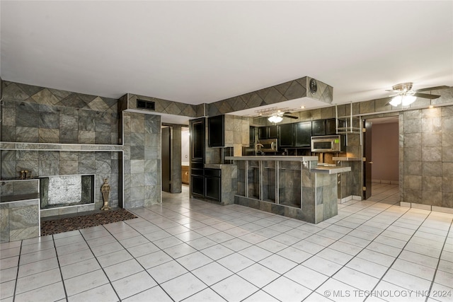 kitchen featuring a tile fireplace, ceiling fan, light tile patterned floors, tile walls, and kitchen peninsula