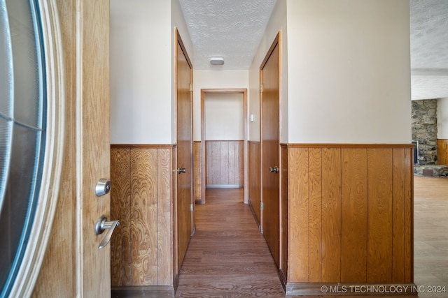 hallway featuring a textured ceiling, light hardwood / wood-style floors, and wooden walls