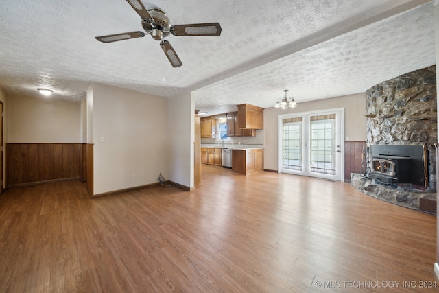 unfurnished living room featuring ceiling fan with notable chandelier, a textured ceiling, light hardwood / wood-style floors, and a wood stove