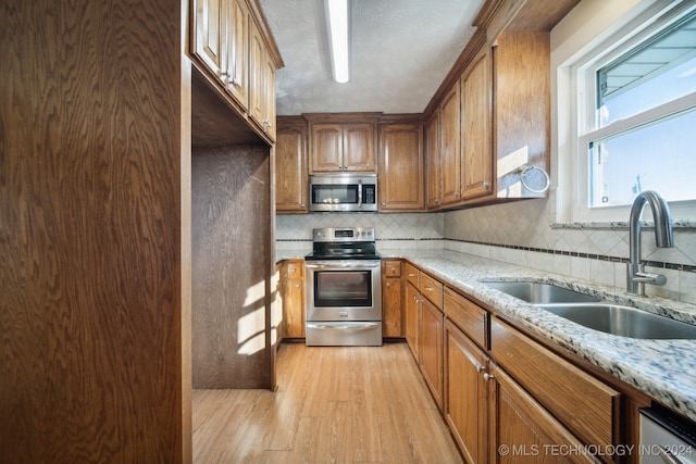 kitchen featuring sink, light hardwood / wood-style flooring, light stone countertops, tasteful backsplash, and stainless steel appliances