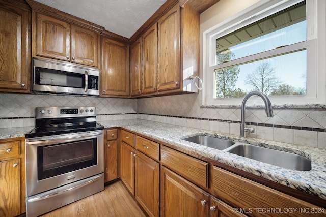 kitchen featuring sink, light hardwood / wood-style flooring, decorative backsplash, appliances with stainless steel finishes, and light stone counters