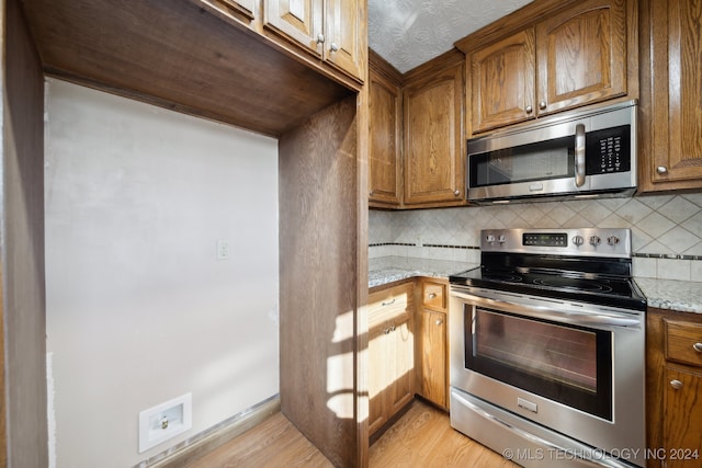 kitchen with decorative backsplash, light wood-type flooring, stainless steel appliances, and light stone counters