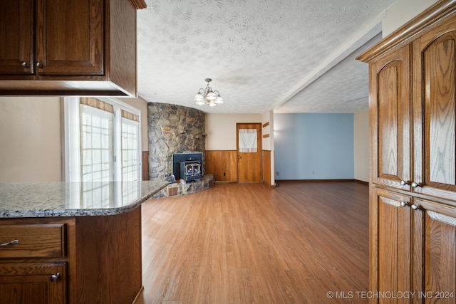 kitchen featuring hardwood / wood-style floors, a wood stove, a textured ceiling, and an inviting chandelier