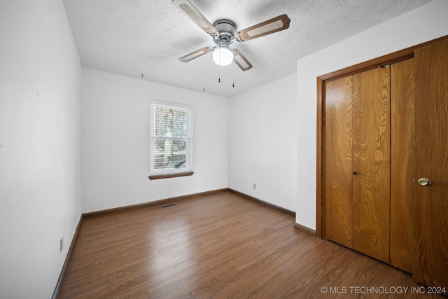 unfurnished bedroom with ceiling fan, a closet, wood-type flooring, and a textured ceiling