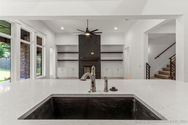 kitchen with a tile fireplace, ceiling fan, sink, light stone counters, and ornamental molding