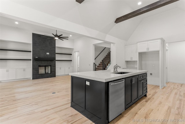 kitchen featuring sink, light wood-type flooring, an island with sink, beam ceiling, and white cabinetry