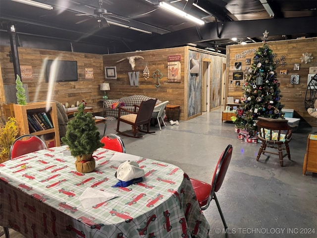 dining room featuring ceiling fan, wooden walls, and concrete floors