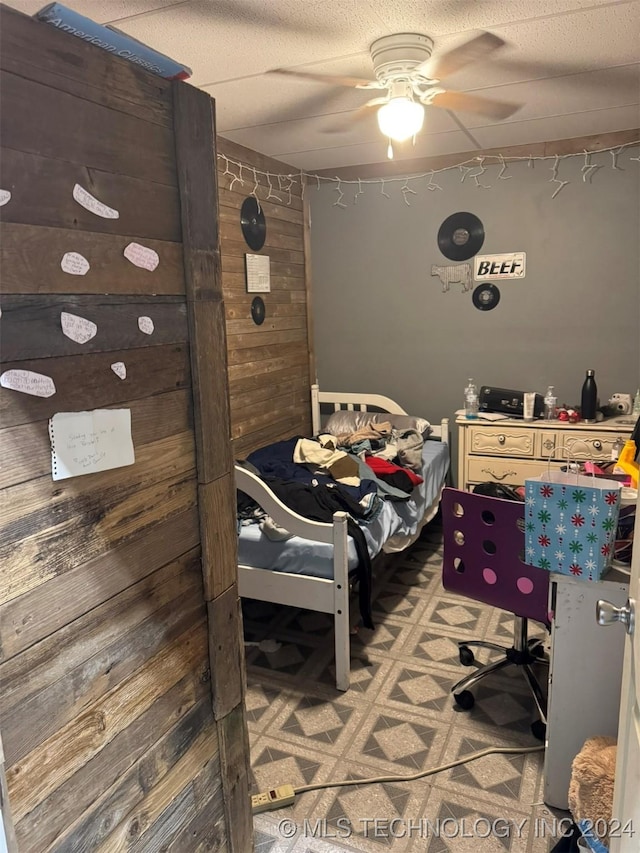 bedroom with ceiling fan and wood walls