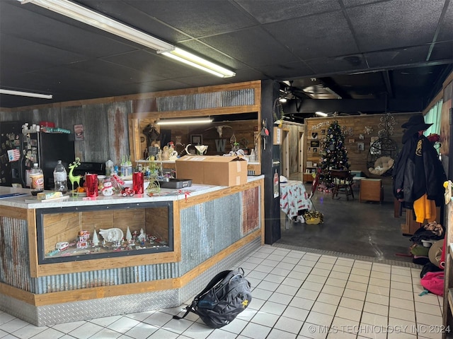 interior space featuring tile patterned floors, a drop ceiling, and wooden walls