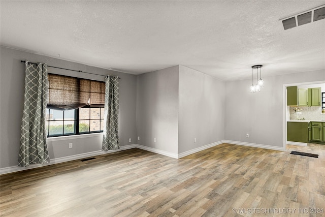 unfurnished room with an inviting chandelier, a textured ceiling, and light wood-type flooring