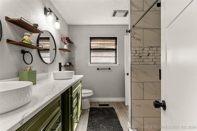 bathroom featuring a tile shower, hardwood / wood-style floors, vanity, and toilet