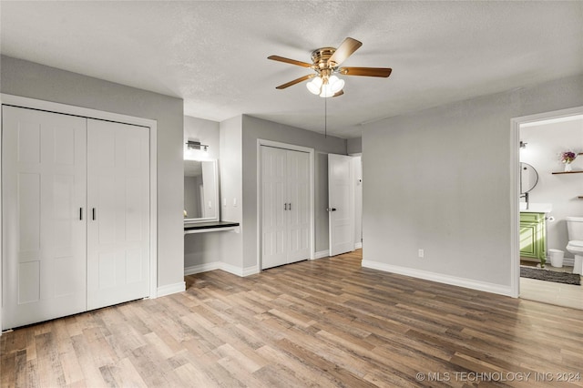 unfurnished bedroom featuring ensuite bathroom, light hardwood / wood-style flooring, ceiling fan, and multiple closets