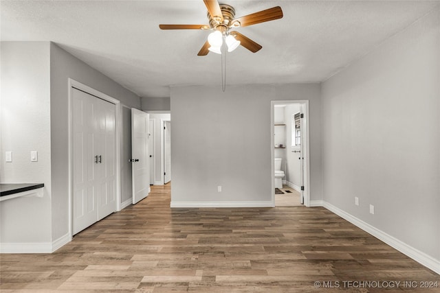 unfurnished bedroom with a textured ceiling, connected bathroom, hardwood / wood-style flooring, and ceiling fan