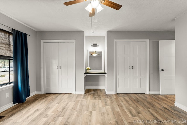 unfurnished bedroom featuring light wood-type flooring, a textured ceiling, and multiple closets