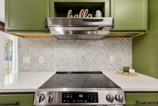 kitchen with green cabinets, light stone counters, stainless steel stove, and exhaust hood