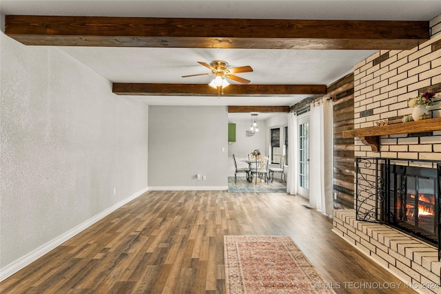 unfurnished living room featuring beam ceiling, ceiling fan, dark wood-type flooring, and a brick fireplace