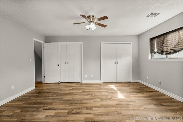 unfurnished bedroom with a textured ceiling, ceiling fan, wood-type flooring, and two closets