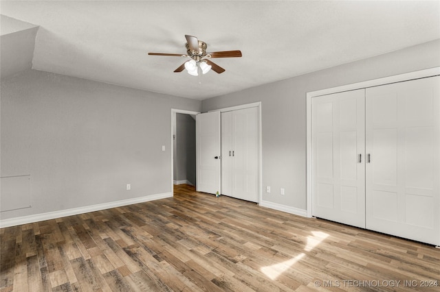 unfurnished bedroom with ceiling fan, vaulted ceiling, wood-type flooring, and multiple closets