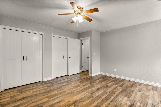 unfurnished bedroom featuring two closets, a textured ceiling, hardwood / wood-style flooring, and ceiling fan