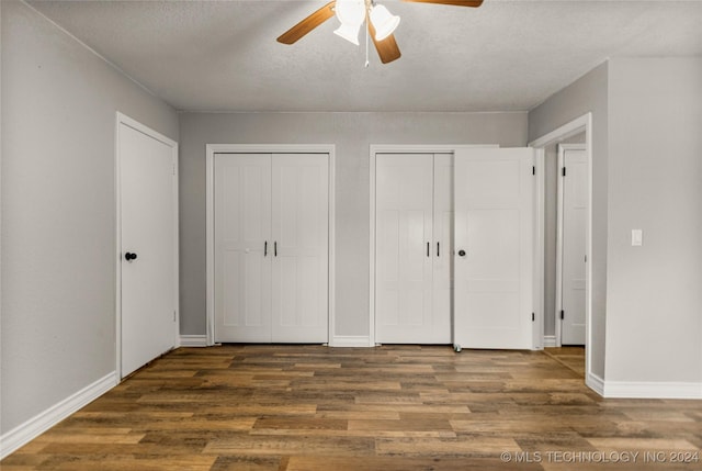 unfurnished bedroom with a textured ceiling, ceiling fan, dark wood-type flooring, and two closets