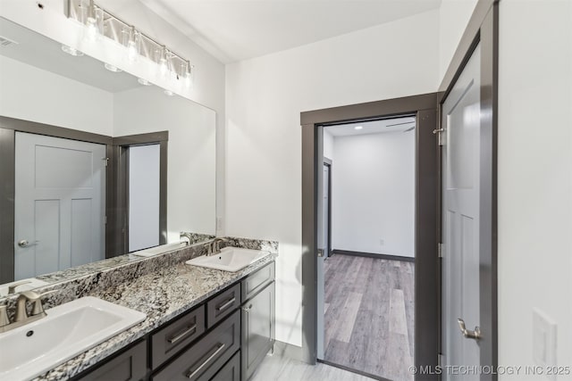 bathroom with wood finished floors, a sink, baseboards, and double vanity